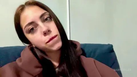 Young woman with long dark hair wearing a brown hoodie in a relaxed indoor setting.
