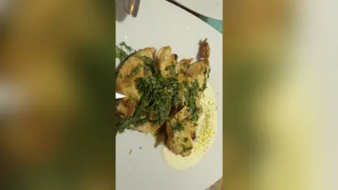 Delicious pan-seared fish fillet topped with fresh green herbs and creamy sauce on a white plate.