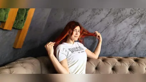 Red-haired woman in a white Dickies t-shirt relaxing on a beige sofa in a modern room.