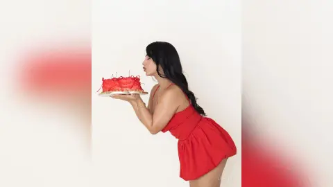 Woman in a red summer dress holding a red cake against a white background with a playful mood.
