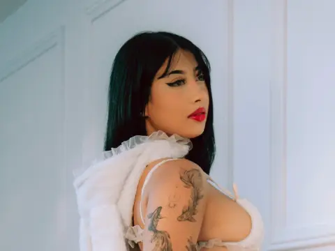 LilithOwens with long black hair and red lipstick poses in a white ruffled top, showing off her fish tattoos.