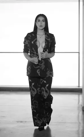 Elegant woman in a patterned black jumpsuit posing confidently in a bright, minimalist studio setting.
