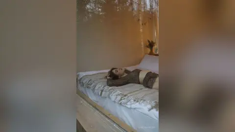 Young woman in a sparkly black bodysuit relaxing on a white bed in a cozy, sunlit bedroom.