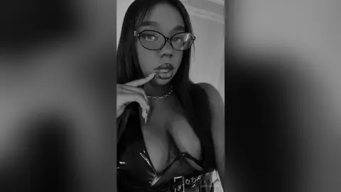 Moody black and white portrait of a woman with glasses and a black top in a minimalist indoor setting.