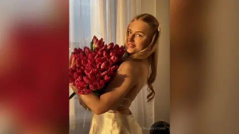 StellaFletcher holds a large bouquet of red tulips against her chest while wearing a white satin dress.