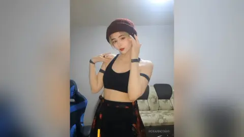 Young woman in a black crop top and maroon beanie posing confidently in a modern living room.