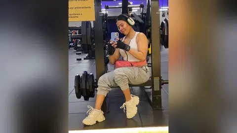 Young woman in white gym outfit taking a selfie in a modern fitness center gym setting.