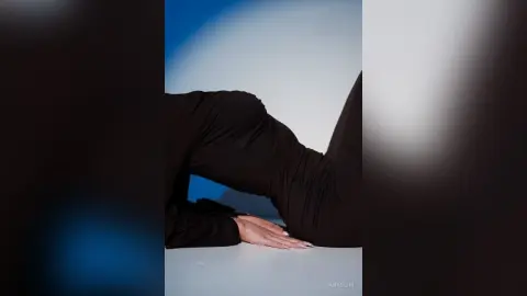 Woman in black leggings performing a yoga stretch on a white floor against a blue sky background.