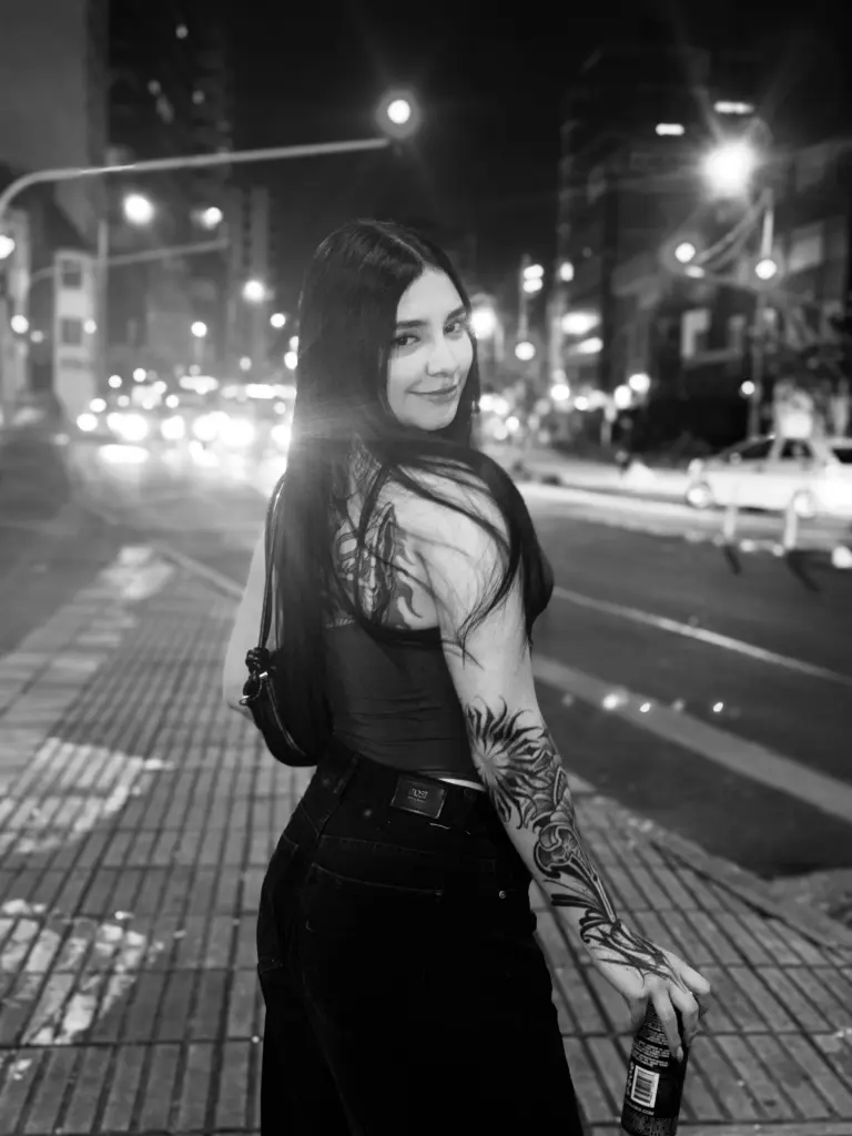 IndiraJhons poses with long black hair and a soft smile, wearing a dark grey scoop-neck top.