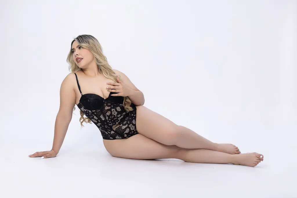 imxkatya poses sideways, showing her long blonde hair and wearing a blue striped button-down shirt and black lace panties.