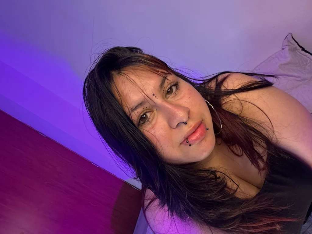 Young woman with dark hair and lip piercing relaxing in moody purple ambient lighting.