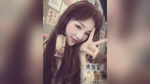 Smiling young woman with long brown hair making a peace sign in a cozy cafe setting.