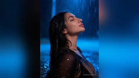 Dreamy portrait of a woman with wet hair standing under blue rain in a moody, cinematic setting.