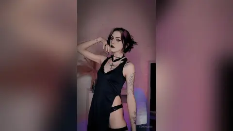 LorenLoiss poses in a black cut-out bodysuit and black choker, showing her tattoos and dark lipstick against a plain wall.