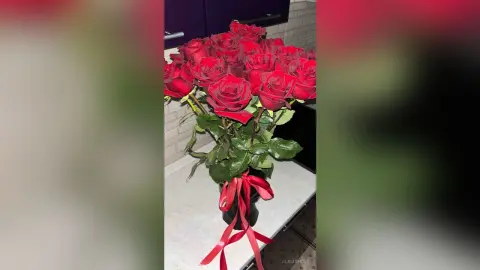 A romantic bouquet of fresh red roses in a glass vase on a white marble countertop.