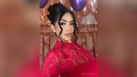Glamorous woman in a red lace dress with elegant updos posing in front of purple party balloons.