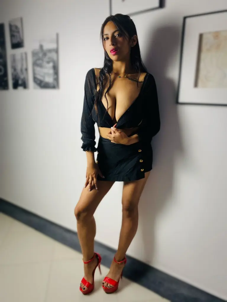 PettryNany poses with long dark hair and red lipstick, showing her bare chest and neck against a light background.