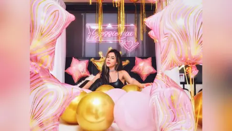 JessieLiu poses behind pink and gold balloons, wearing a black lace bra and a black choker.