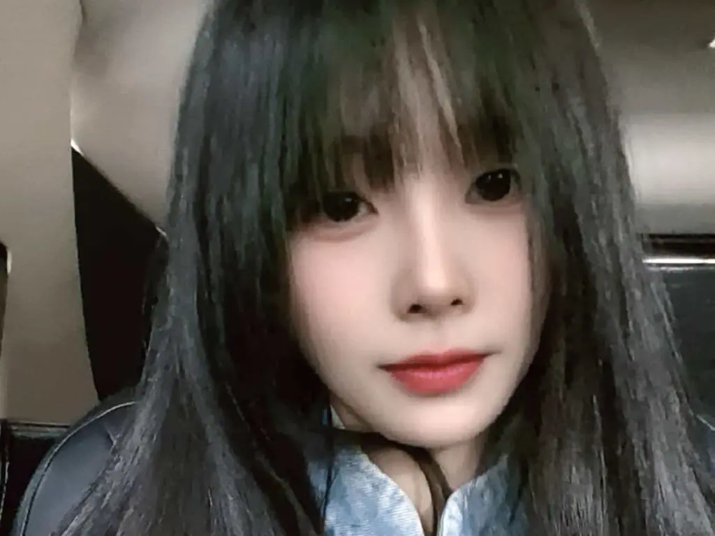 Young woman with long black hair and bangs wearing a blue shirt in a car setting with a soft, calm mood.