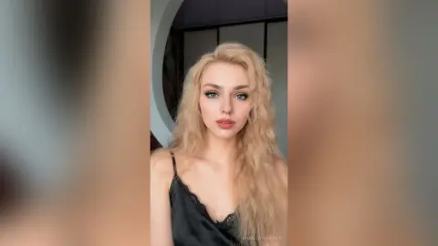 CharlotteReimer with long blonde wavy hair wearing a black lace camisole looking at the camera.