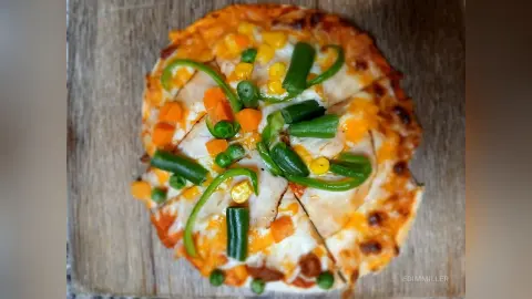 Delicious homemade veggie pizza topped with green beans and corn on a rustic wooden serving board.
