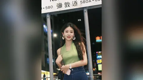 Smiling young woman in a green halter top and jeans standing on a city street at night.