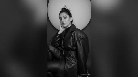 Elegant woman in a chic black leather outfit posing against a minimalist circular backdrop in a moody portrait.