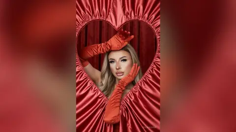 Blonde woman in red satin gloves posing inside a red heart-shaped frame for a romantic Valentine's Day mood.
