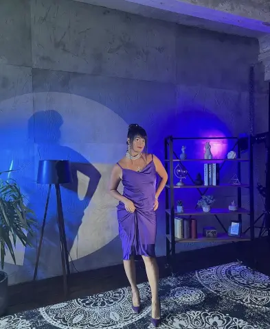 Elegant woman in a purple satin slip dress posing in a moody, blue-lit modern studio setting.