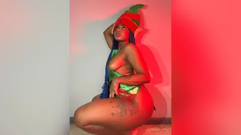 Curvy woman in a green elf costume and red hat posing against a pink background with festive mood.