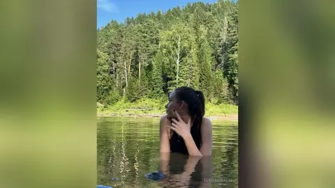 Young woman in black swimwear relaxing in a calm forest lake surrounded by lush green trees.