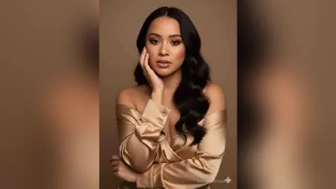 Elegant woman in a gold satin off-the-shoulder dress posing against a warm brown studio background.
