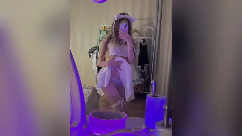 Young woman in a white lace co-ord set taking a mirror selfie in a bedroom with soft purple lighting.