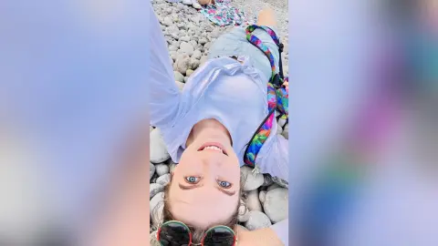 Smiling young woman in a white shirt relaxing on a sunny rocky beach during a summer vacation.