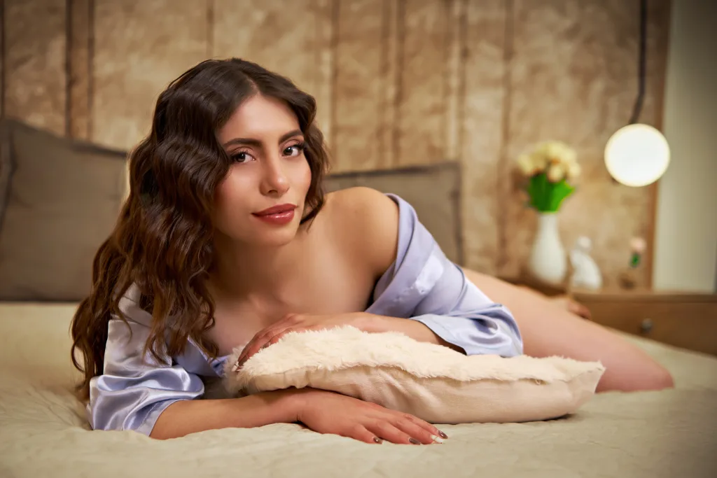 CelesteVoss — CelesteVoss lies on a bed wearing a light purple satin robe with her long wavy hair falling over her shoulder.