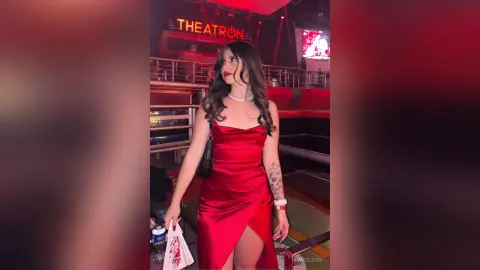Elegant woman in a red satin cocktail dress posing at a nighttime Theatron event.