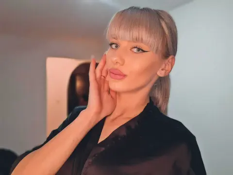 Blonde woman with bangs in a black satin top posing with a soft, elegant expression indoors.