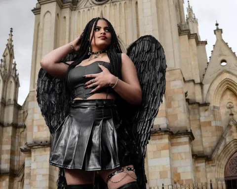 Woman in black leather outfit and large feathered wings posing in front of a gothic cathedral.