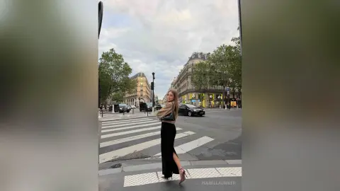 Stylish woman in a black maxi skirt and beige sweater walking on a Parisian street under a cloudy sky.