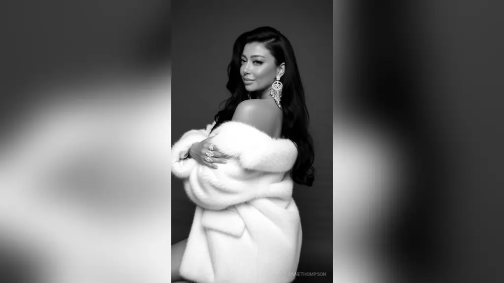 AnneThompson — Elegant woman in a white faux fur coat and statement earrings posing in a glamorous black and white studio portrait.