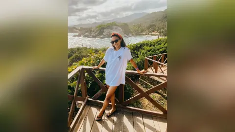 Smiling woman in white t-shirt and sunglasses relaxing on a wooden pier by a tropical ocean coastline.