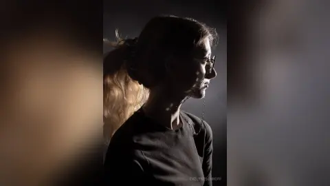 Moody profile portrait of a blonde woman in a black shirt wearing glasses in dramatic studio lighting.