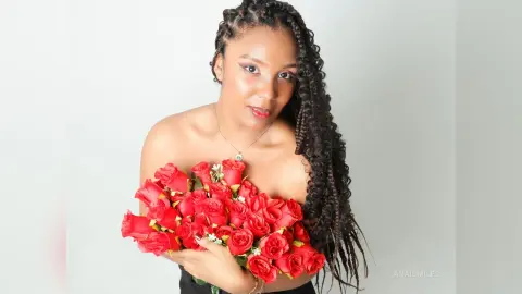 Smiling Black woman with long braids holding a large bouquet of red roses against a white background.