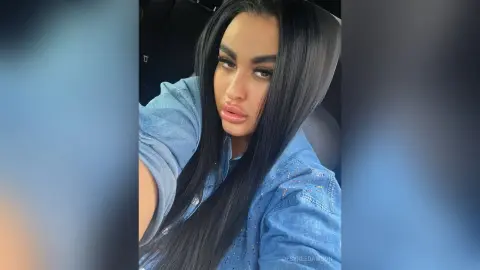 Young woman with long dark hair wearing a blue denim shirt sitting in a car for a casual selfie.