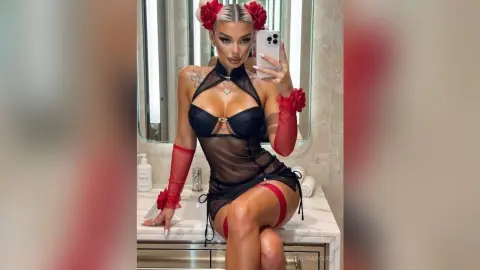 Glamorous woman in a black sheer lace bodysuit and red gloves posing in a marble bathroom.