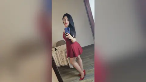 Young woman in a stylish red mini dress taking a mirror selfie in a modern bedroom setting.