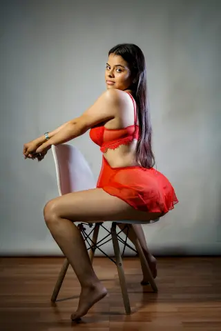 Young woman in red lace lingerie sitting on a white chair in a studio setting with a soft mood.