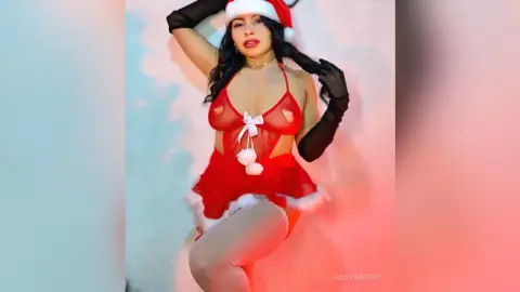 Glamorous woman in a red and white sexy Santa outfit and black gloves posing in a festive holiday setting.