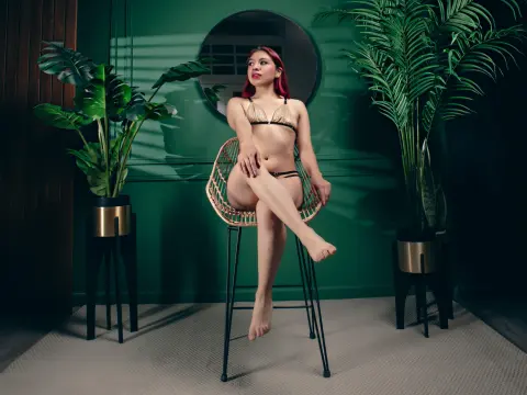 Fashionable woman in a gold bikini sitting on a rattan chair in a moody green room with tropical plants.
