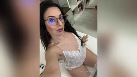 Smiling woman in white lace lingerie relaxing on a bed in a bright bedroom.